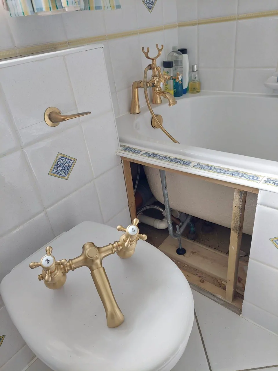 A new brass tap set laid out beside a bath with its panel removed for access to the pipework