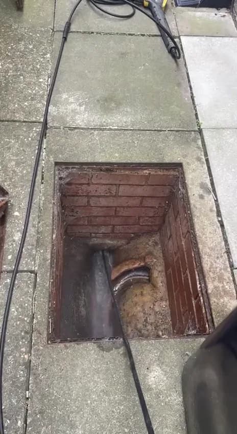 A high-pressure hose feeding down the channel of an open inspection chamber in a paved path