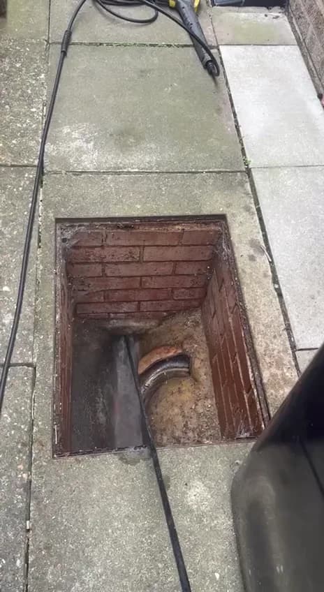 A jetting hose running into a brick inspection chamber with its cover lifted