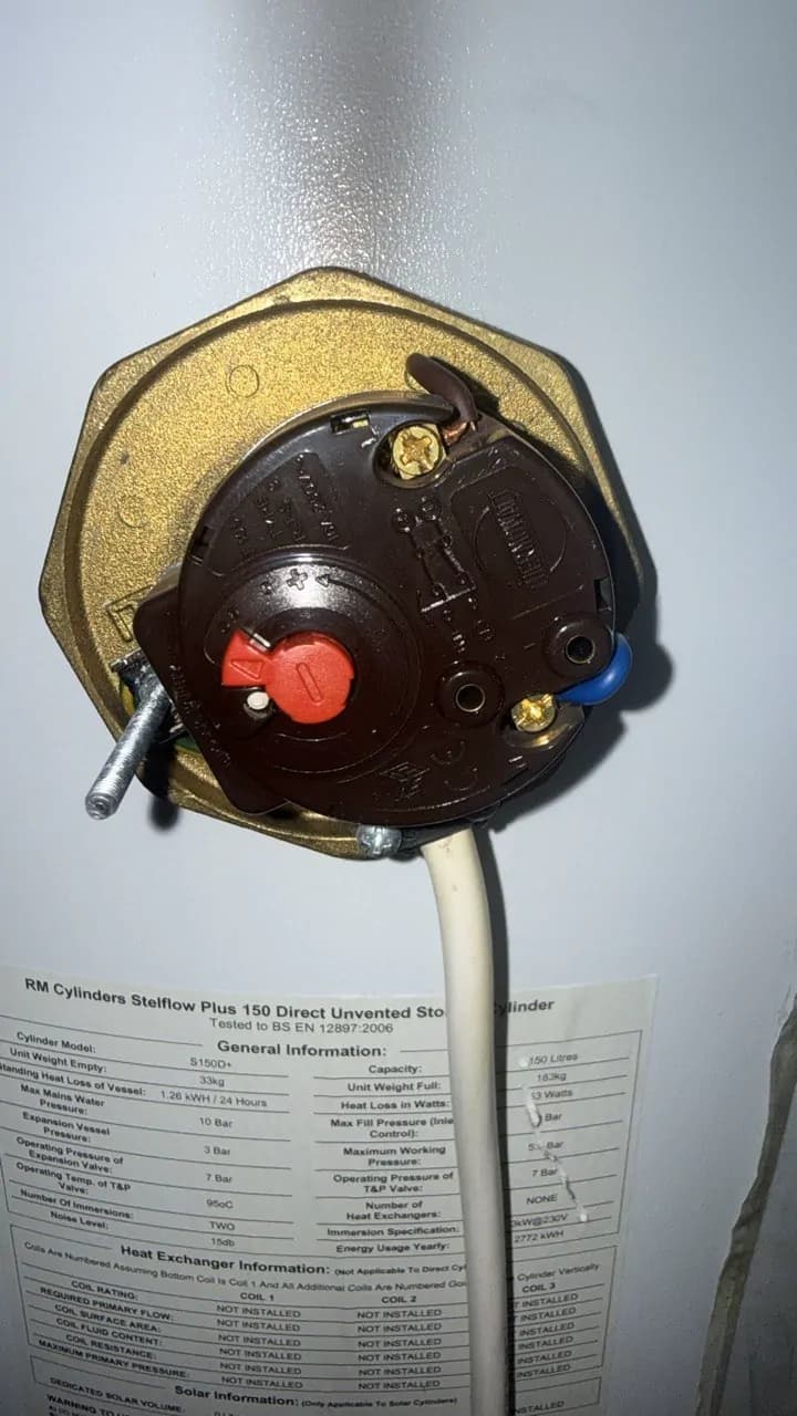 The thermostat of an immersion heater with its cover off, mounted on a hot water cylinder