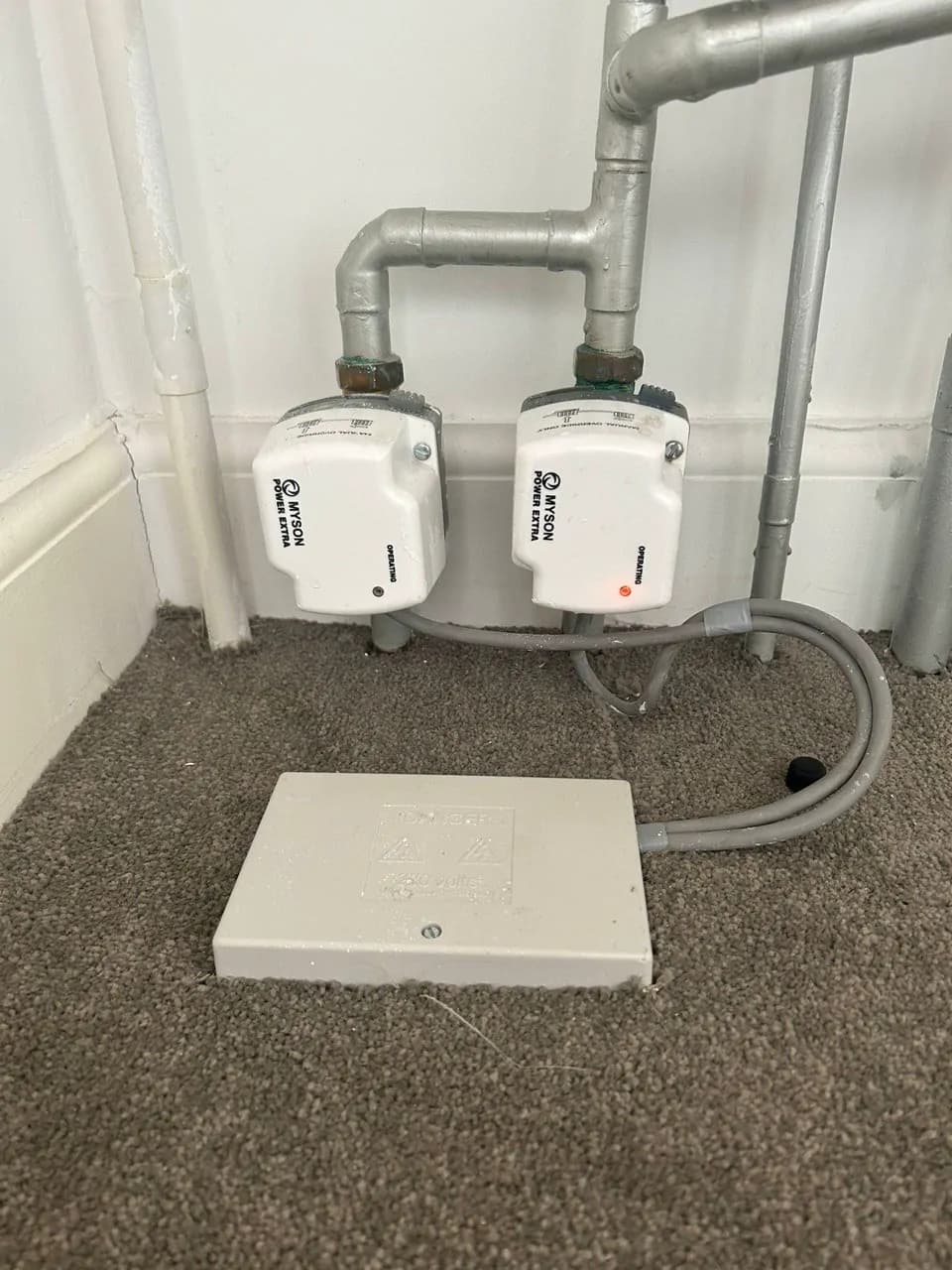 Two white motorised valves fitted to painted steel pipes above a carpeted floor