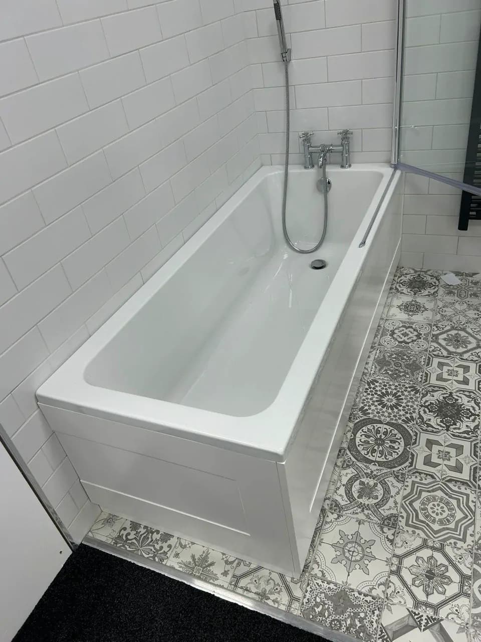 A new white bath with chrome mixer taps and a shower hose, fitted against white tiled walls