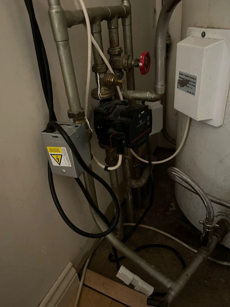 A pump, a gate valve and pipework in a cupboard beside a hot water cylinder