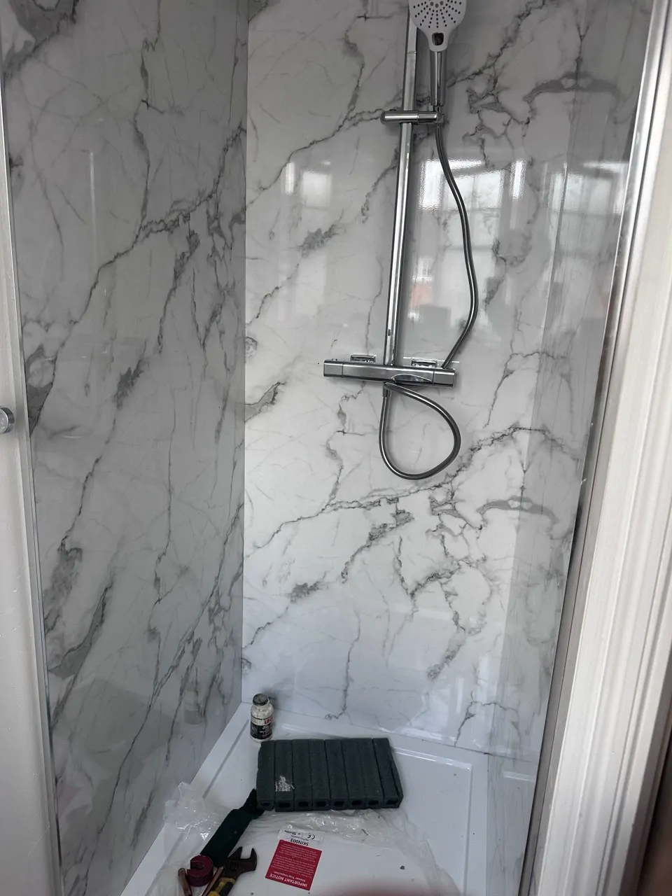 A new shower enclosure with marble-effect wall panels and a chrome shower, tools still in the tray
