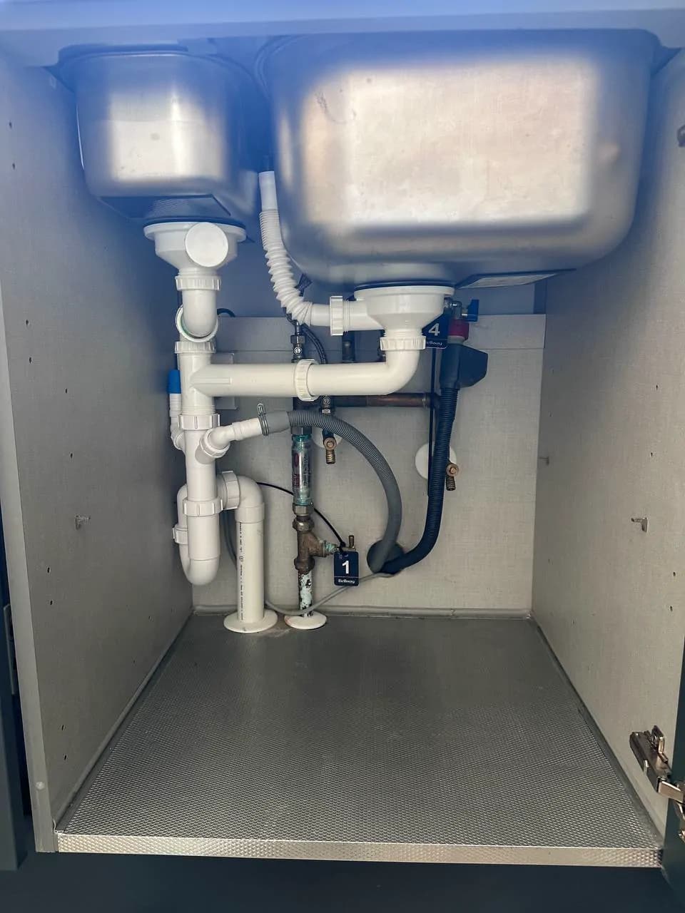 White waste pipes, traps and isolation valves neatly plumbed under a double kitchen sink