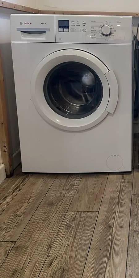A white washing machine plumbed in under a worktop on a wood-effect floor